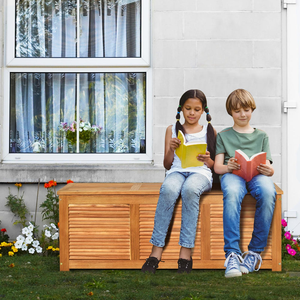 Acacia wood storage bench box with children reading, offering 46-gallon capacity for outdoor patio or garden use.