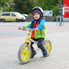 Child riding a green 12-inch balance bike with adjustable seat and rotatable handlebar on a paved surface.