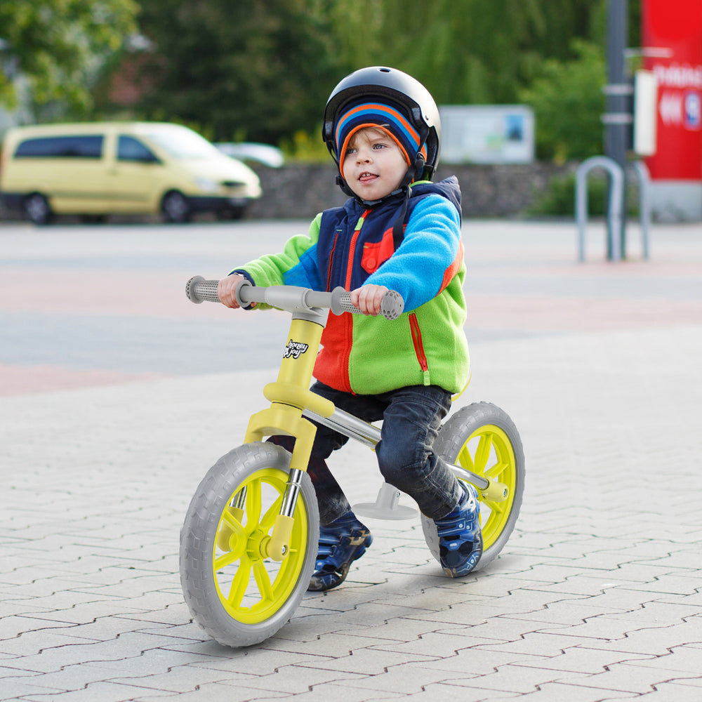 Child riding a green 12-inch balance bike with adjustable seat and rotatable handlebar on a paved surface.