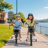 Two girls riding 12-inch kids bikes with training wheels along a scenic pathway by the water, promoting outdoor fun.
