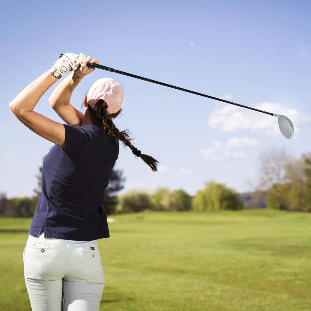 Woman swinging a 12° individual driver golf club for women with a lightweight graphite shaft on a sunny golf course.