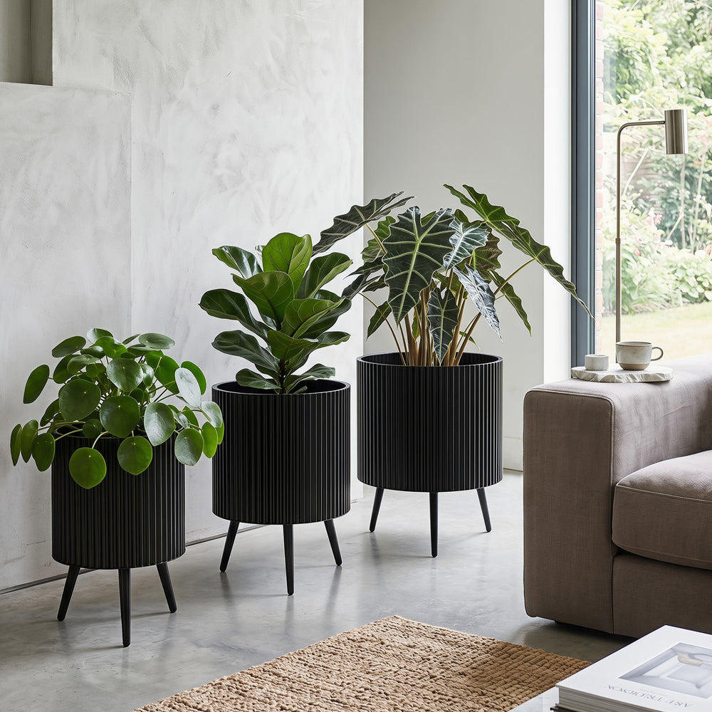 Fluted black metal plant pots with tapered legs, ideal for indoor or outdoor use, enhancing plant growth and decor.