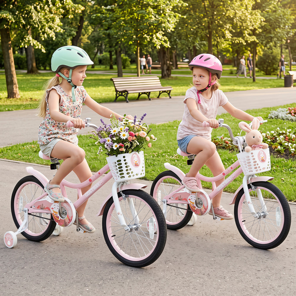 Two girls riding 18-inch pink kids' bikes with adjustable seats, front baskets, and training wheels in a park.