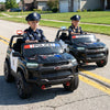 Two kids in a black 24V 2-seater ride-on police car with LED lights, designed for ages 3 to 8, on a road.