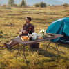 6 feet folding portable rattan table with carrying handle, set up outdoors for picnics and gatherings.