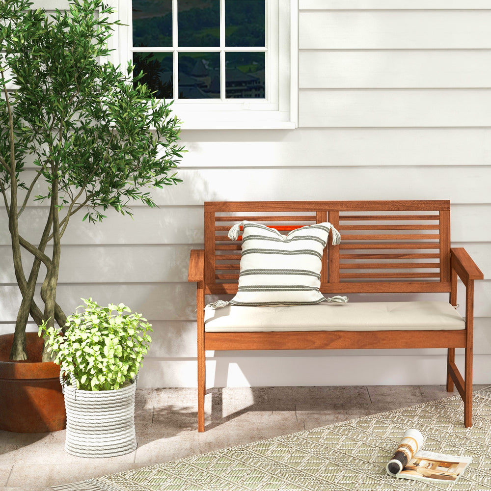 Solid wood patio bench with backrest and cushion, designed for two, perfect for backyard or balcony relaxation.