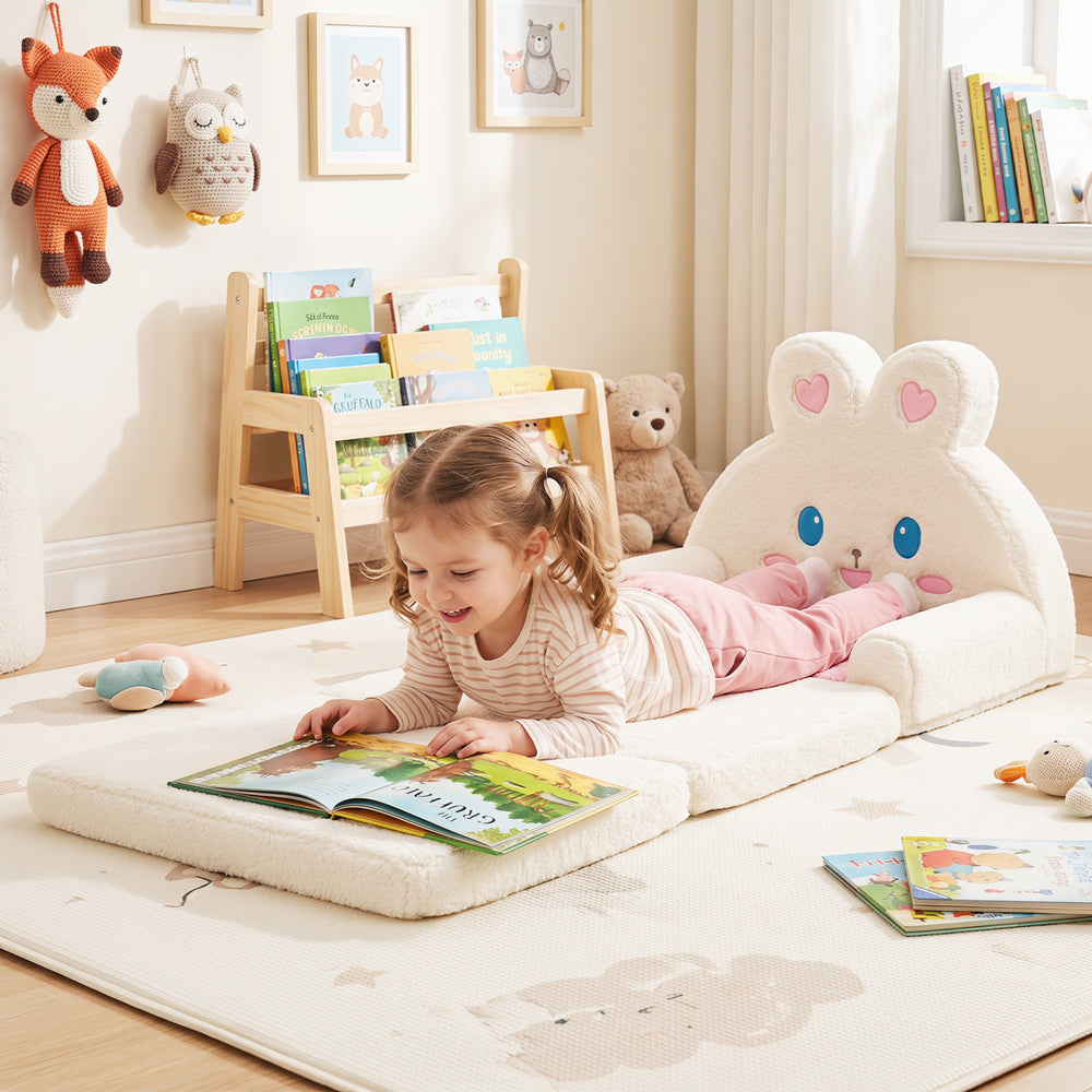 Convertible kids sofa in pink with bunny pattern, used as a lounger for reading in a cozy playroom setting.