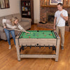 Swivel game table in brown with foosball and pool features, designed for 2-4 players, shown in a living room setting.