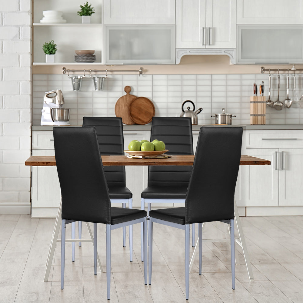 Four black PVC leather dining side chairs with painted steel legs around a wooden table in a modern kitchen setting.
