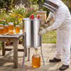 3 frame manual honey extractor in stainless steel with clear lid, used for home apiary honey extraction outdoors.