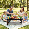 Folding camping table in black, set up for a picnic with family, featuring drinks and snacks on a grassy area.