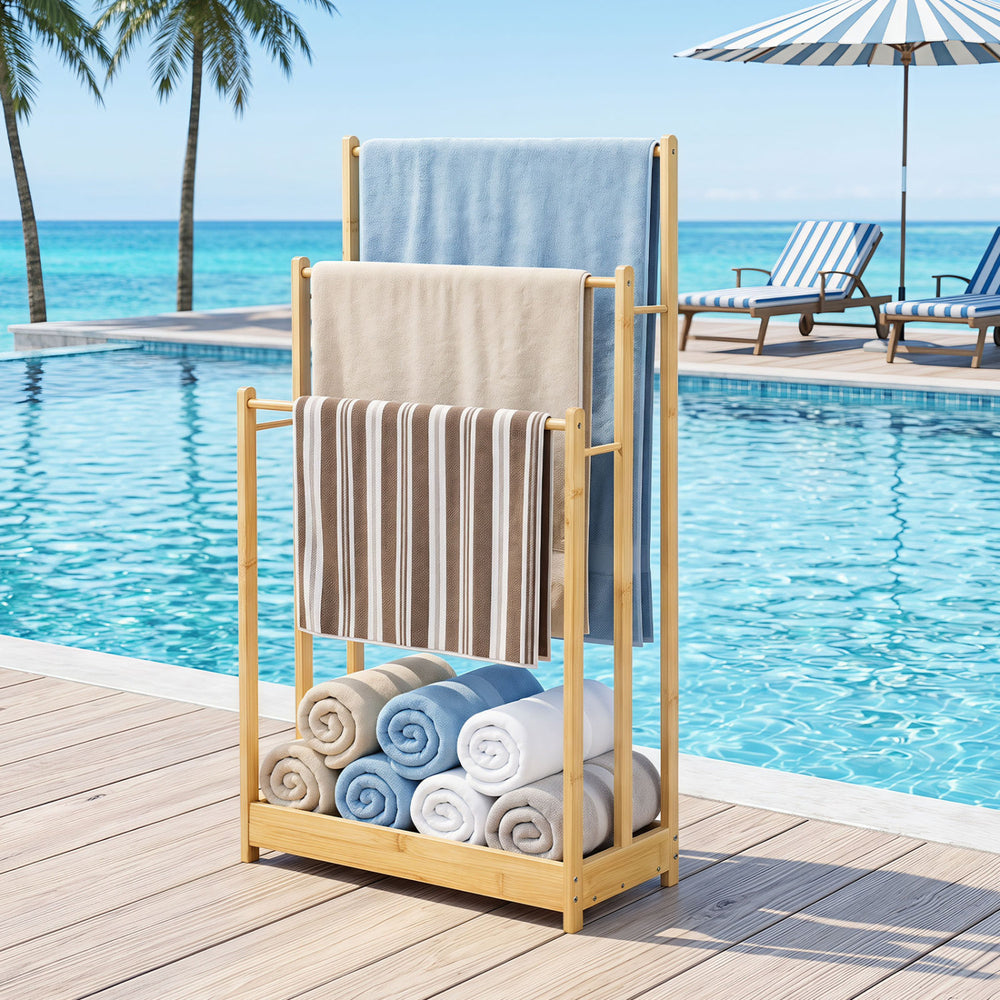 Three-tier free-standing bamboo towel rack with storage shelf, ideal for drying towels by the poolside.