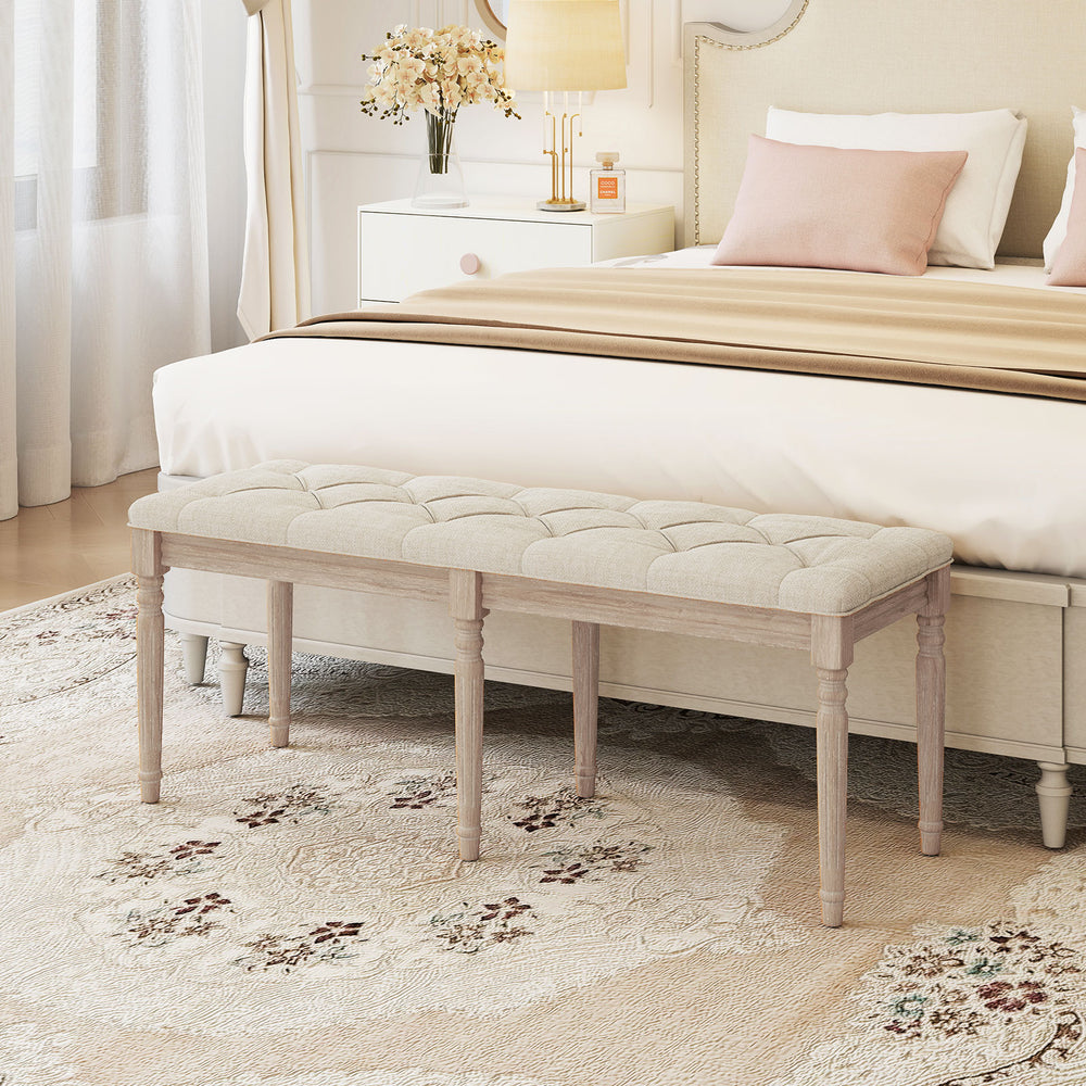 Upholstered bench with button-tufted seat and carved rubber wood legs, ideal for bedroom or living room seating.