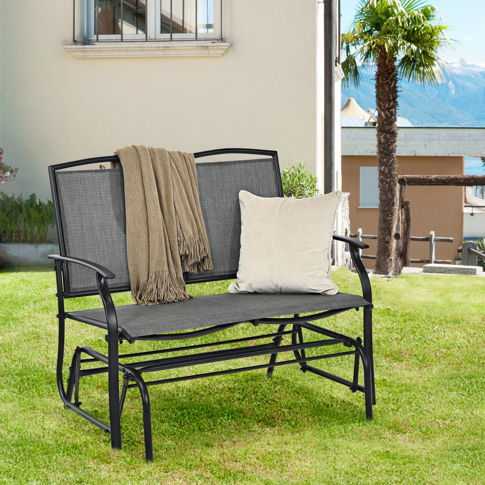 Gray iron patio rocking chair with a cozy blanket and pillow, perfect for outdoor relaxation in your backyard.