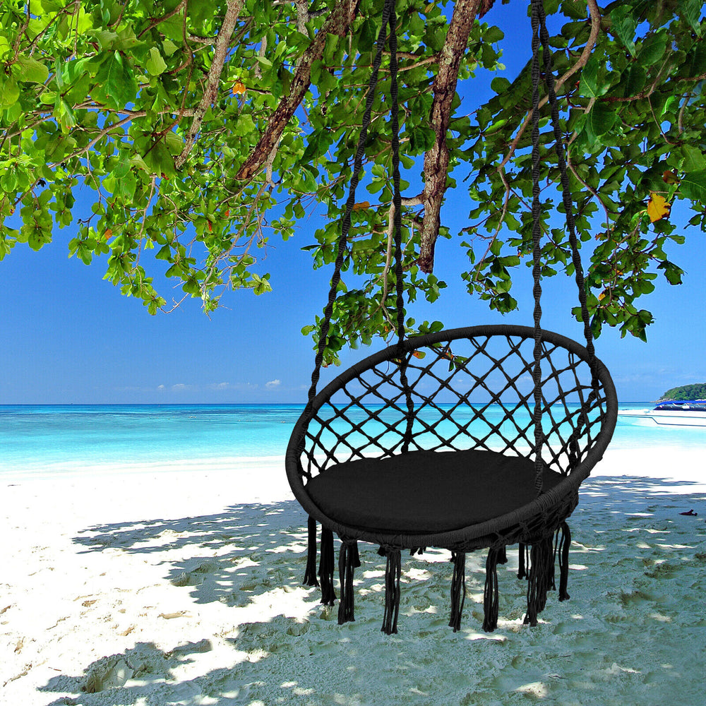 Cushioned black hammock swing chair hanging under a tree, perfect for outdoor relaxation by the beach.