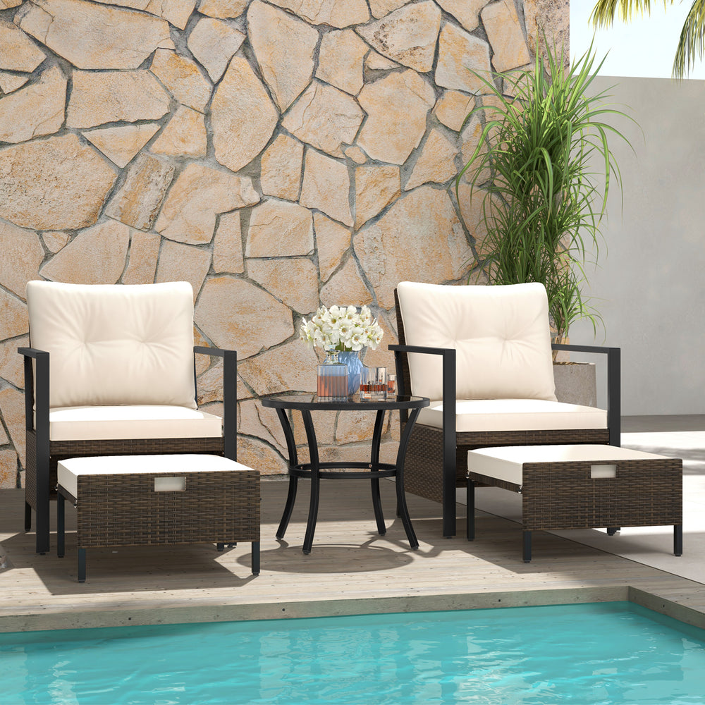 Two cushioned chairs and ottomans in a 4-piece outdoor furniture set with a glass-topped coffee table, perfect for.
