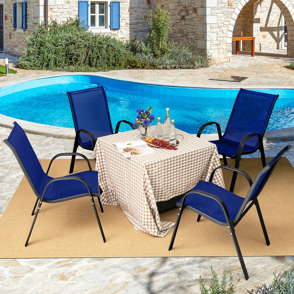 Four navy stackable patio dining chairs with armrests arranged around a table by a pool, perfect for outdoor dining.