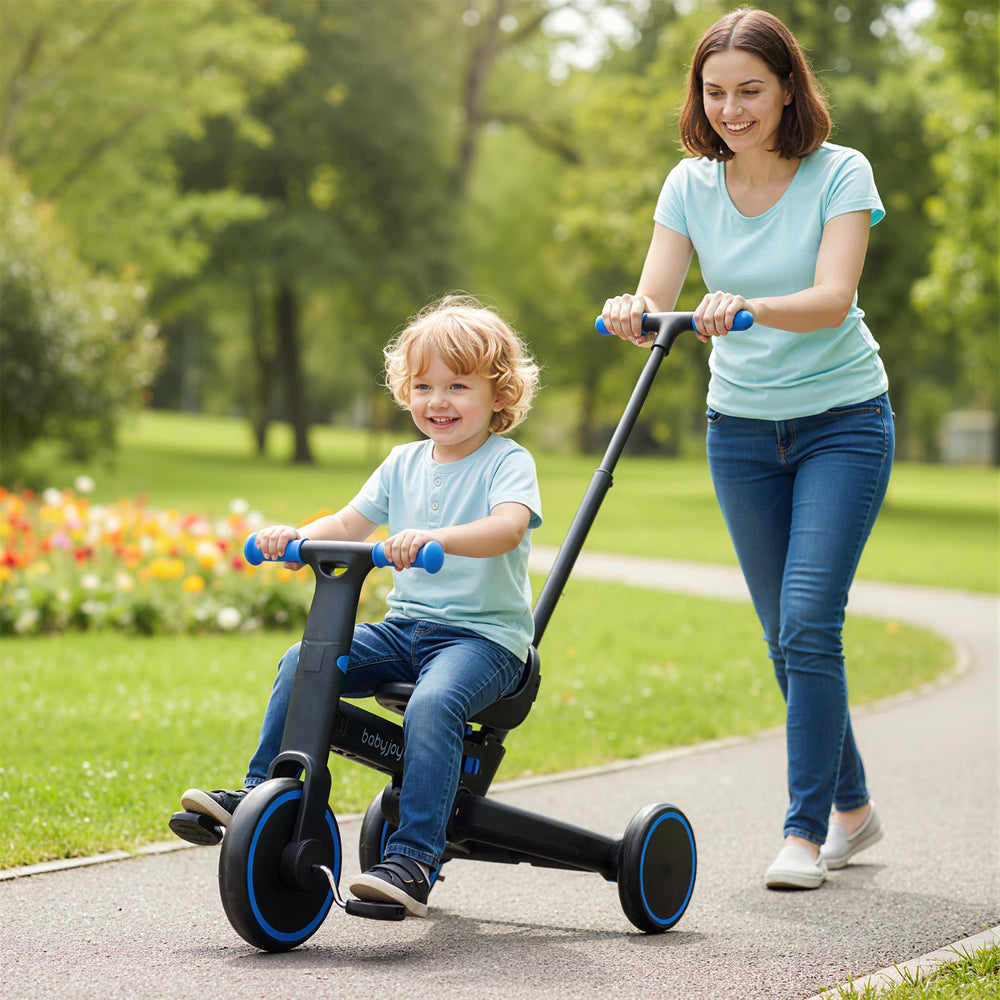 Toddler riding the navy 4-in-1 foldable tricycle with push handle, designed for safety and comfort in a park setting.