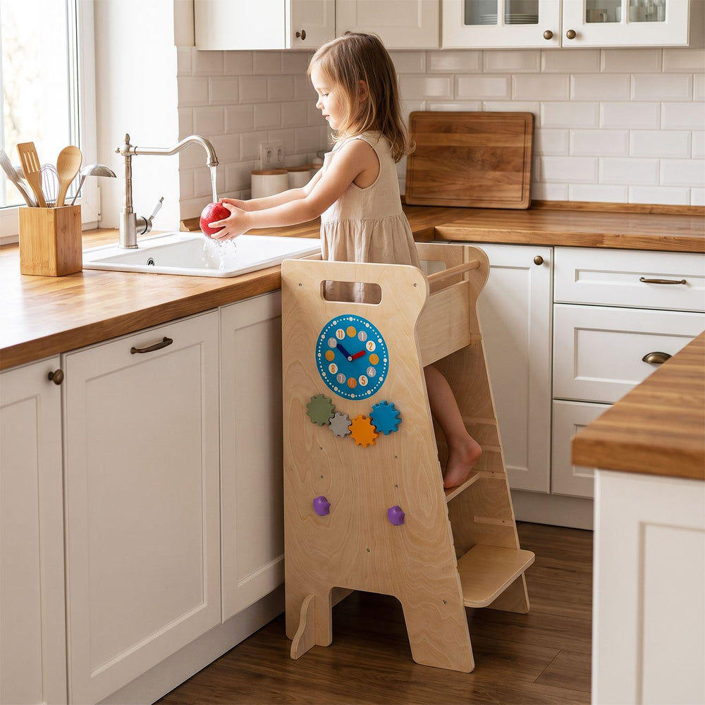 Toddler tower with adjustable height and Montessori games shown in a kitchen, with a child washing an apple at the sink.