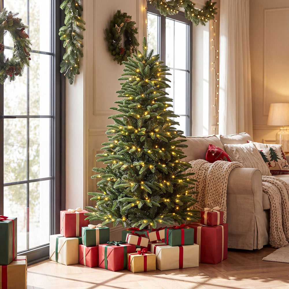 Pre-lit artificial Christmas tree with warm LED lights and three gift boxes, perfect for festive indoor celebrations.