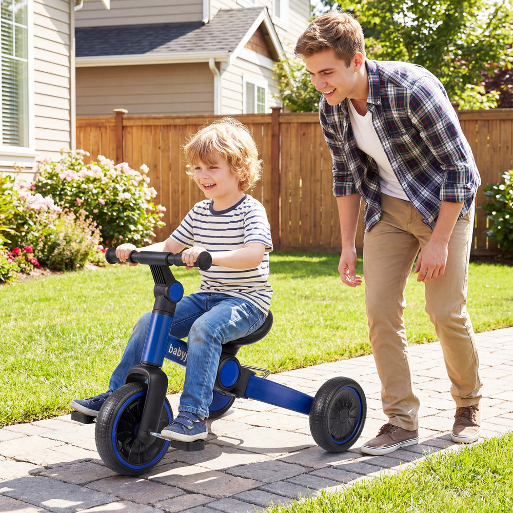 Toddler riding a blue 5-in-1 balance bike with removable pedals, guided by an adult in a backyard setting.