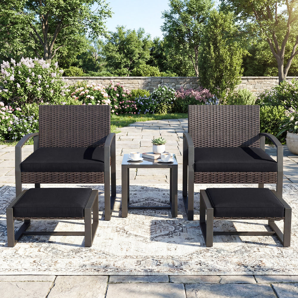 Two black cushioned chairs with ottomans and a tempered glass side table in a patio setting for outdoor relaxation.