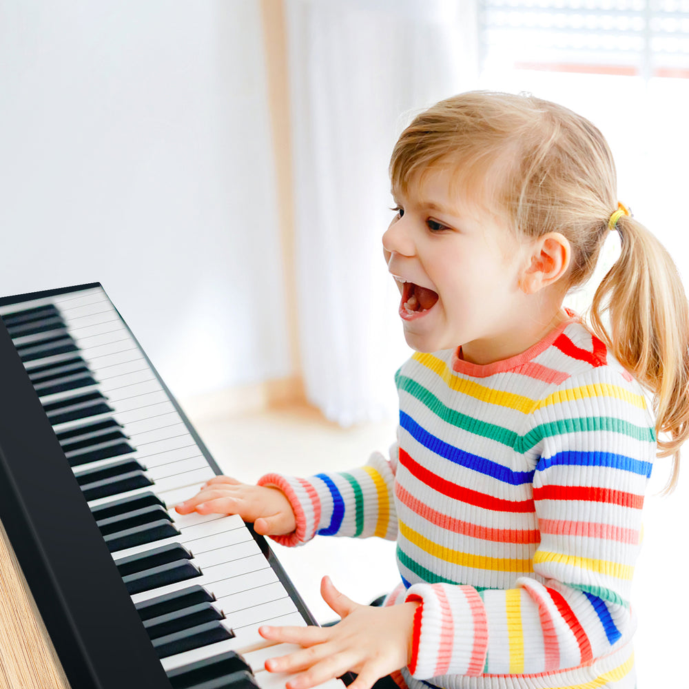 Child playing the 61-key folding piano keyboard in black, showcasing full-size keys and a joyful expression.