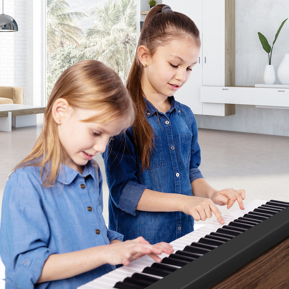 Two children playing a 61-key folding piano keyboard in a bright room, showcasing its full-size keys and portable.