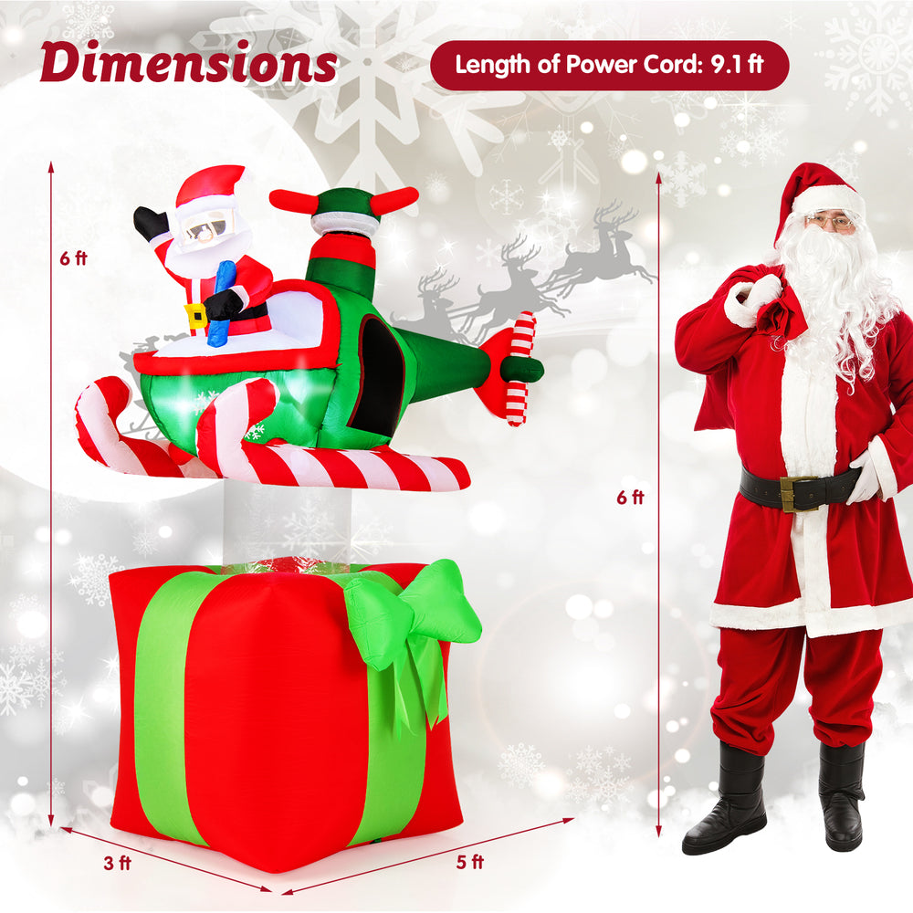 Santa Claus pilots a 6-foot inflatable airplane with LED lights, landing on a large red gift for festive outdoor decor.