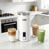 6-in-1 electric milk steamer in white with stainless steel interior, serving multiple cups of rich foam beverages.