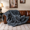Gray faux wolf fur blanket draped over a brown sofa, featuring a soft plush texture for cozy warmth and comfort.