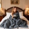 Soft plush gray faux wolf fur blanket draped over a bed, ideal for cozying up on sofas or armchairs.