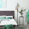 Retro floor lamp with three amber glass shades, placed beside a bed, adding elegant lighting to a cozy bedroom setting.
