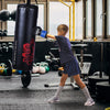 Child practicing boxing with a filled punching bag, featuring gloves and a sturdy PU design for durability.