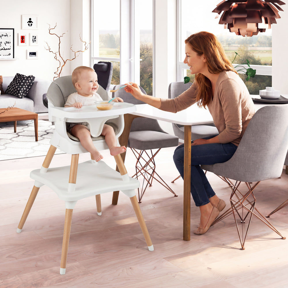 Convertible high chair in white with solid wood legs, featuring a baby seated and enjoying a meal at the dining table.