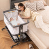 Gray baby bassinet bedside sleeper with clear height adjustment indicators and lockable wheels for safe, versatile use.