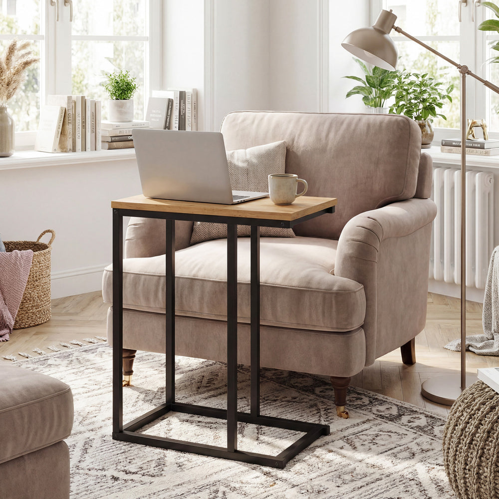 C-shaped end table with a sturdy metal frame and natural wood top, ideal for use beside a chair in a living room.