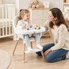 Convertible high chair in beige with a 5-point harness, featuring a removable tray and beech wood legs for stability.
