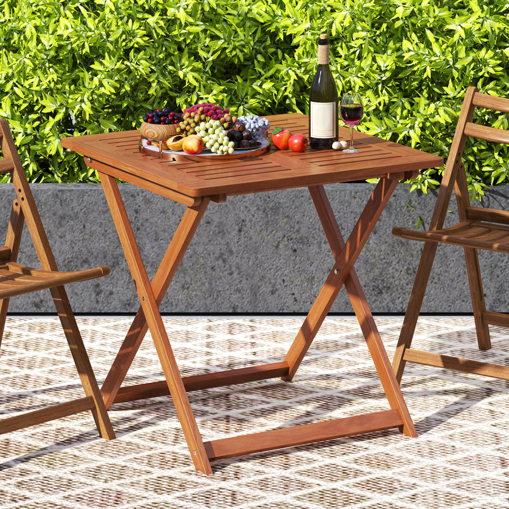 Square patio dining table with teak finish, umbrella hole, and folding design, perfect for backyard or poolside use.