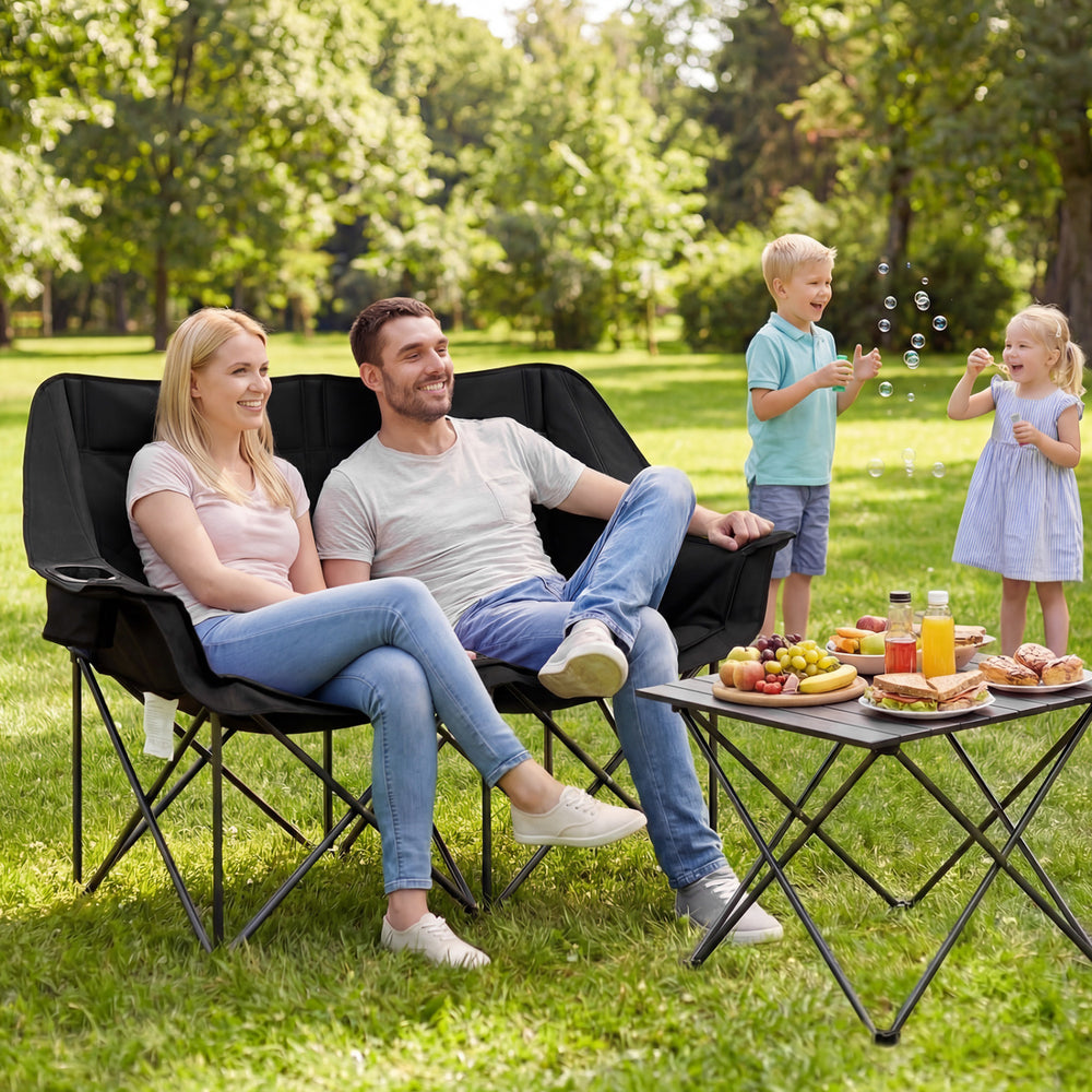 Double camping chair in black with cup holders, featuring a padded backrest, ideal for outdoor picnics and relaxation.