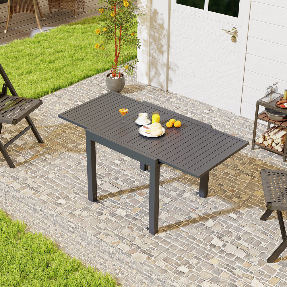 Expandable grey patio dining table for 4-6 people with slatted top, set on a stone patio for outdoor gatherings.