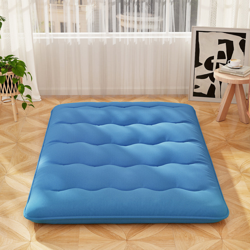Blue foldable futon mattress with washable cover, ideal for camping or as a floor mat, shown in a cozy indoor setting.