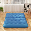 Blue foldable futon mattress with washable cover, ideal for camping or as a floor mat, shown in a cozy indoor setting.