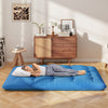 Blue foldable futon mattress with washable cover, shown in a cozy indoor setting, ideal for camping or home use.