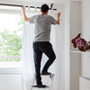User standing on a folding 2 step ladder with anti-slip pedals, adjusting curtains in a bright room. Ideal for home.