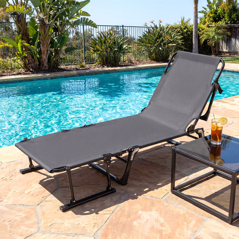 Gray folding camping cot chaise lounge chair by the pool, featuring a heavy-duty metal frame and removable cushion.