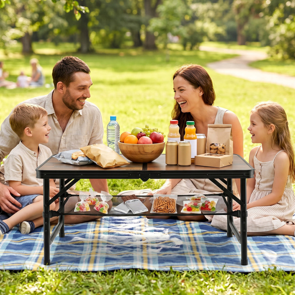Folding camping table in black and brown, set for a picnic with family on grass, featuring adjustable heights and.