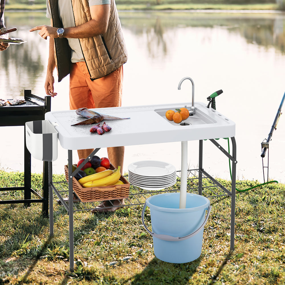 Folding fish cleaning table with sink and faucet, featuring a spacious tabletop and side trash bag holder for BBQ use.