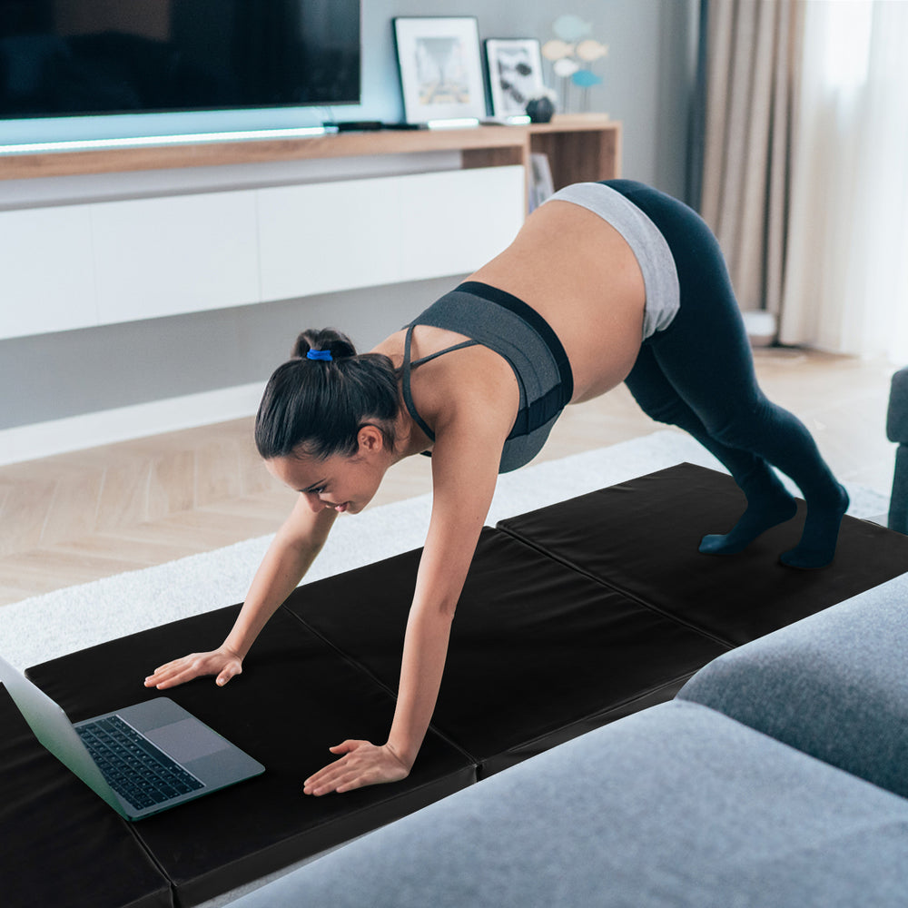 Folding gymnastics mat in black with a woman practicing yoga, featuring a sweatproof PU leather cover and carry handles.