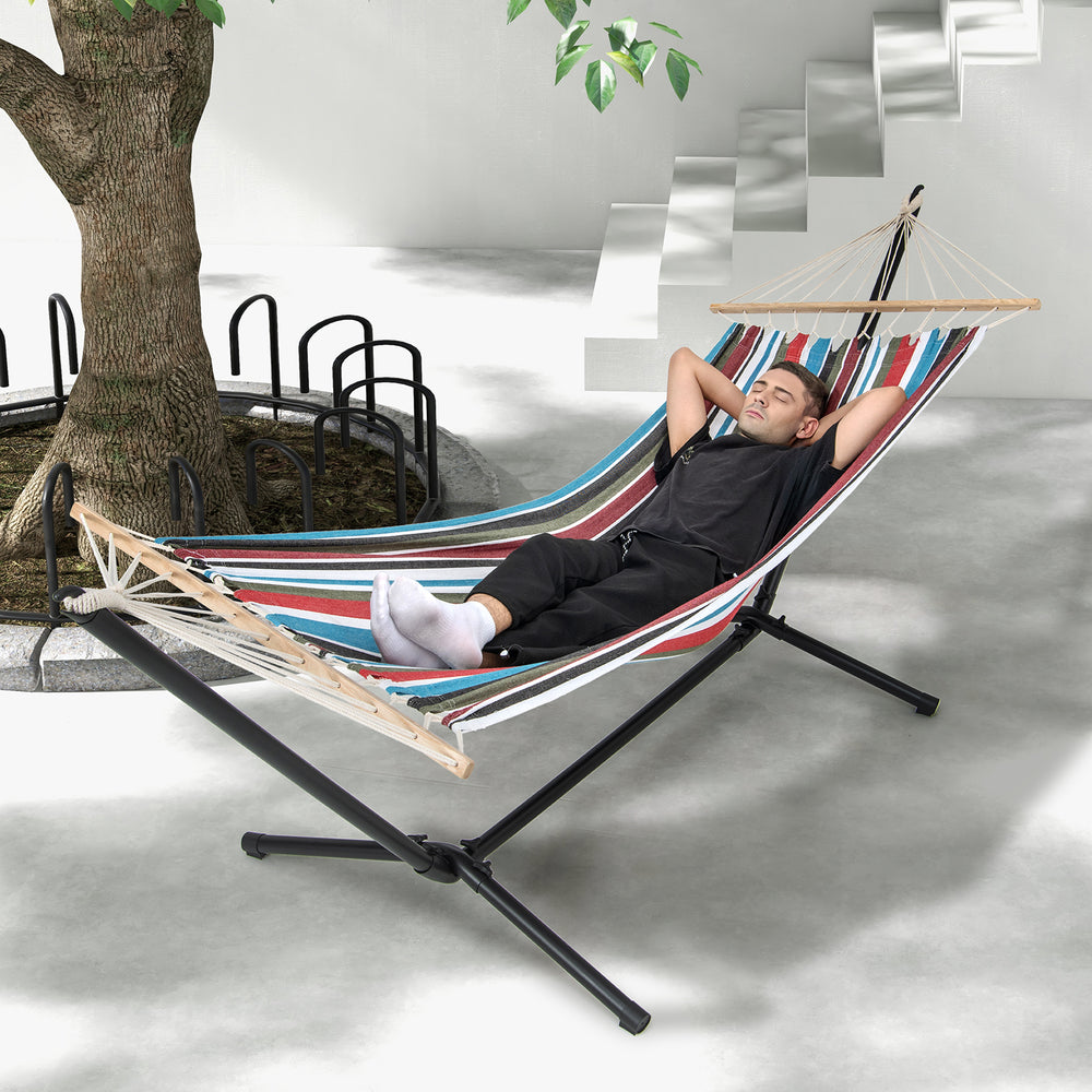 Multicolor hammock with stand, featuring breathable fabric and wood spreader bar, perfect for relaxing in the backyard.